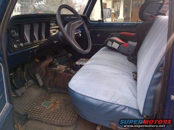 1978 Ford Bronco interior showing dashboard, steering wheel, bench seat with child seat, and floor pedals. Supermotors.net logo visible