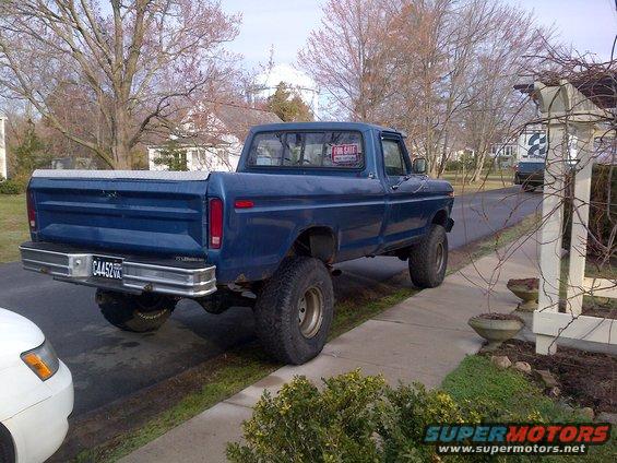 Blue pickup truck with "FOR SALE" sign in window, lifted suspension, and aftermarket wheels