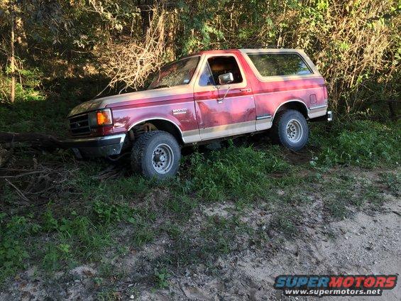 Red and tan Ford Bronco parked on a dirt path with trees and brush