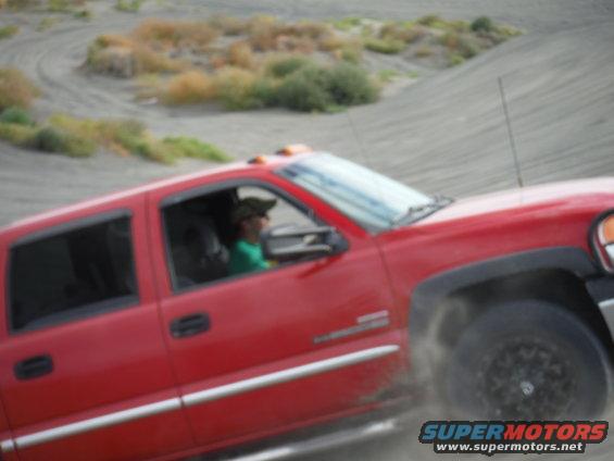 Red pickup truck with a person driving, kicking up dust on a sandy terrain