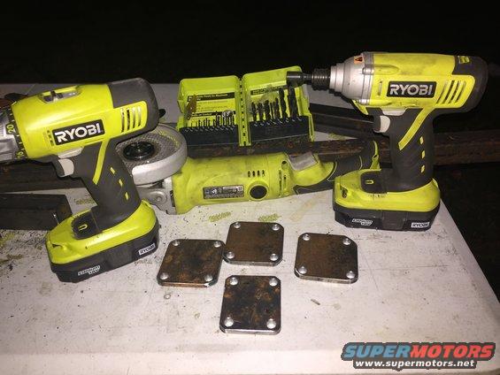 Four rusty metal plates with four bolts each, two Ryobi drills, an angle grinder, and a drill bit set on a white surface