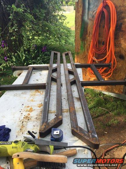 Two metal sliders with triangular bracing, a tape measure, and a power tool on a workbench