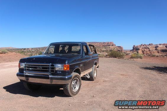 Dark blue Ford Bronco parked on a dirt road with red rock formations in the background