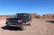 1989 Ford Bronco - A dark blue Ford Bronco is parked on a dirt road with a desert landscape and red rock formations under a clear blue sky.