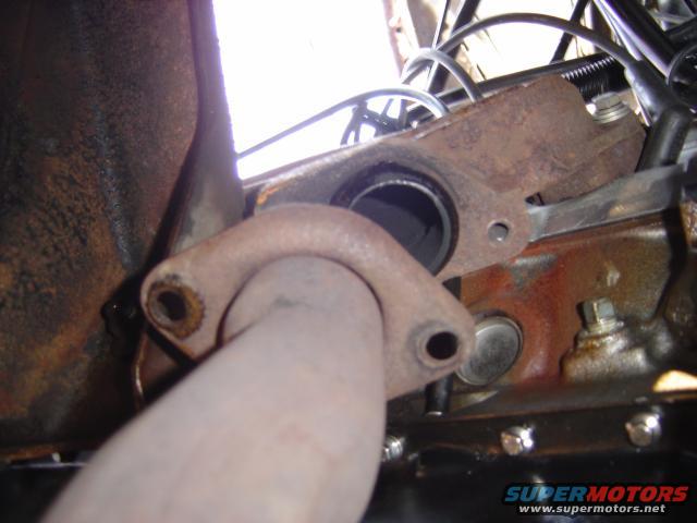 Exhaust manifold and pipe connection on an engine, showing rust and bolts