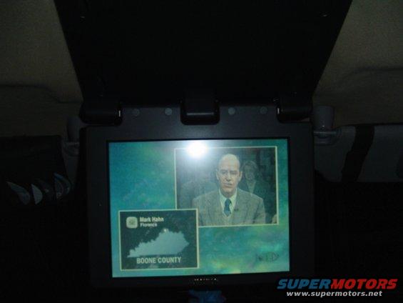 Car interior screen displays a news report with a man in a suit and a map of Boone County, Kentucky