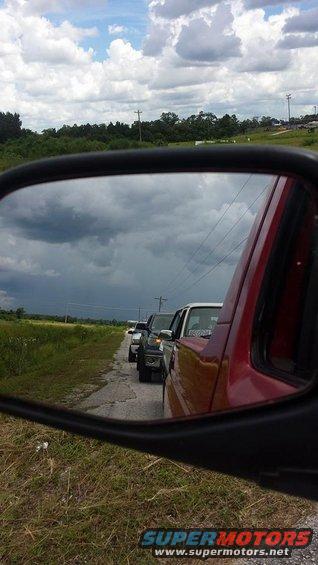 Line of trucks seen in side mirror, red vehicle in foreground