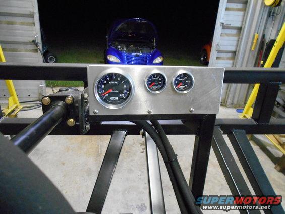 Custom gauge panel with tachometer, oil pressure, and water temperature gauges. Blue car in background