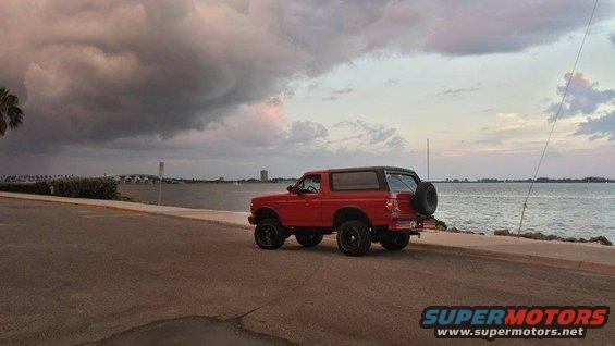 Red 1995 Ford Bronco parked by the water with a stormy sky