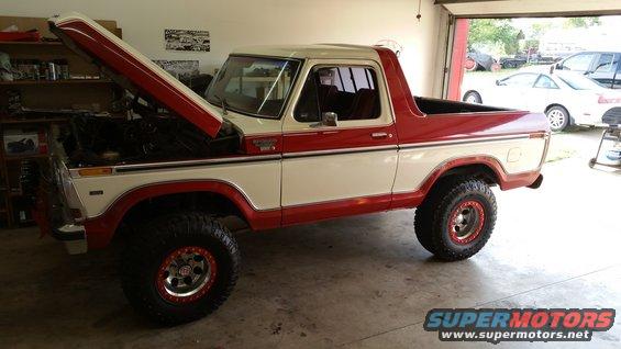 Two-tone red and white Ford Bronco with hood open, parked in a garage