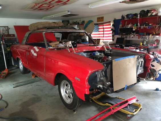 Red coupe with hood open, front end disassembled, on jack stands in a garage