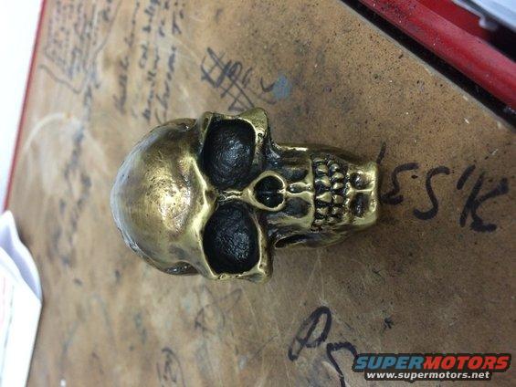 Brass skull part on a workbench with handwritten notes