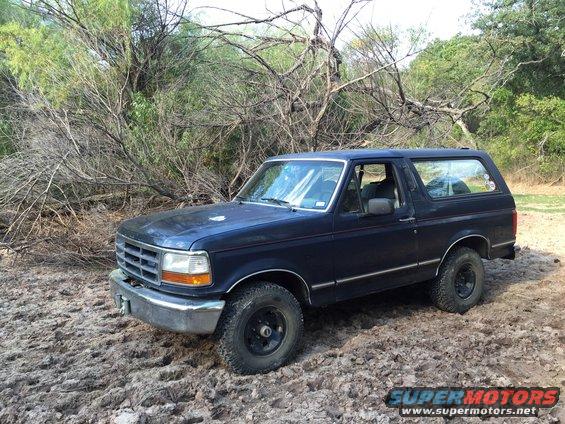 1993 Ford Bronco parked on muddy ground with trees in background