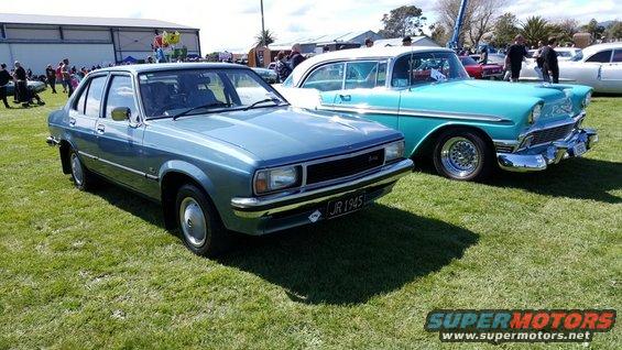 Blue sedan and turquoise classic car parked on grass at an outdoor event