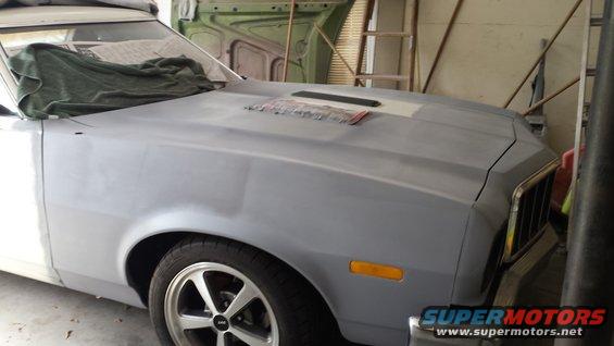 Gray primer Ford Ranchero with a scoop on the hood, seen from the front 3/4 angle