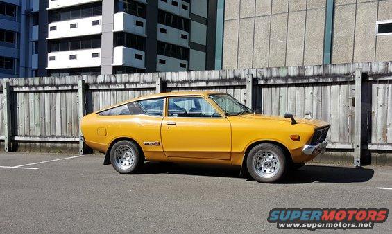 Yellow Datsun coupe parked outside a building, side view