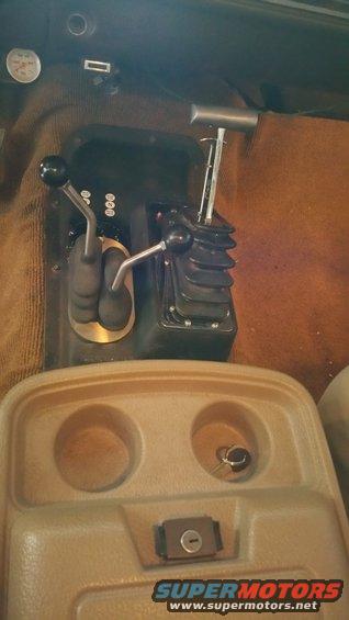 Interior shot of a vehicle's center console with two shifters, a gauge, and cup holders. A key is in one of the cup holders
