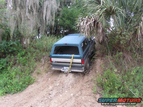 Blue Ford Bronco with a camper shell on a dirt trail, stuck in mud
