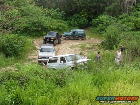 White 1996 Ford Bronco in tall grass with other vehicles nearby