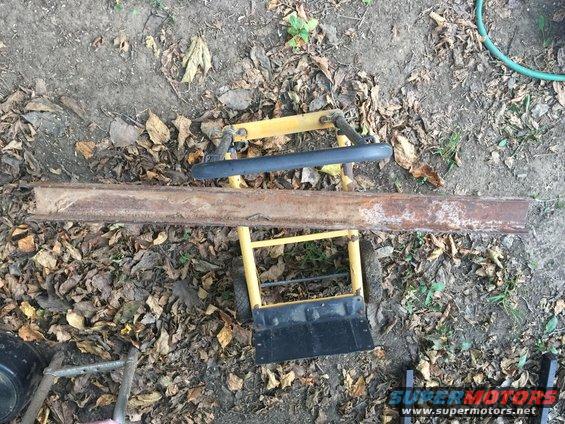 Rusty metal beam resting on a yellow dolly with black handles and wheels