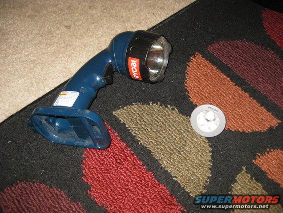 Blue Ryobi flashlight with orange logo and a small round Philips light on a patterned rug