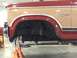 1984 Ford Bronco - The front fender and door of a two-tone Ford Bronco are visible as the vehicle is raised on jack stands.