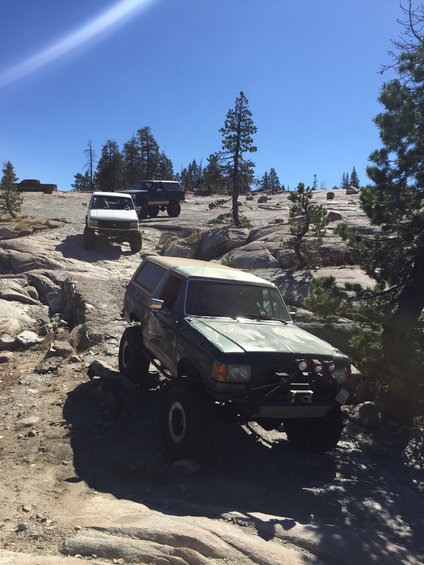 Green SUV with lifted suspension and off-road tires navigating rocky terrain