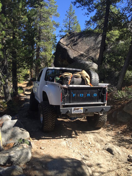 Ford pickup truck with large tires on a rocky trail, bed loaded with gear