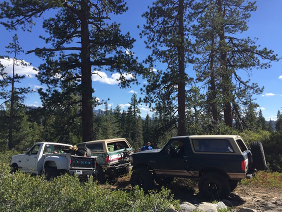 Dark green Ford Bronco with a tan top and spare tire on the back, angled right, on a rocky trail