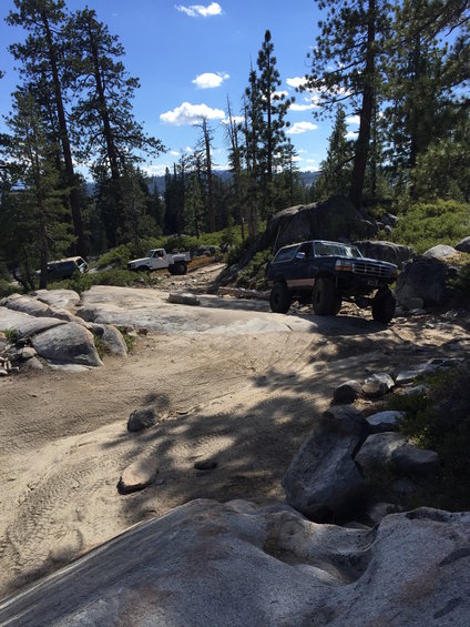 1989 Ford Bronco navigating a rocky off-road trail with other trucks in the background