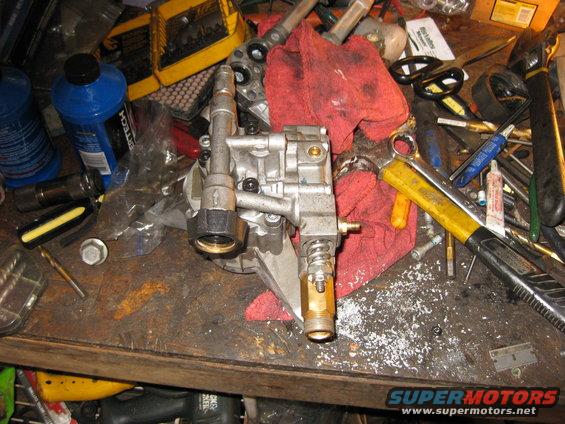 Pressure washer pump on a cluttered workbench with tools and rags