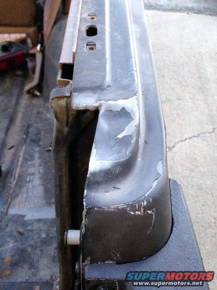 Close-up of a dented and scraped metal edge of a vehicle door, showing primer and chipped paint