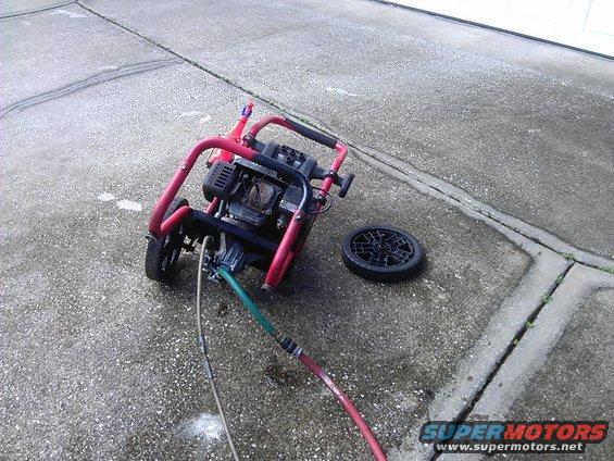 Red frame pressure washer with black engine and detached wheel on concrete
