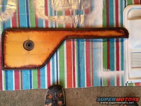 Orange car door panel with rusty edge and a circular cutout, lying on a striped blanket