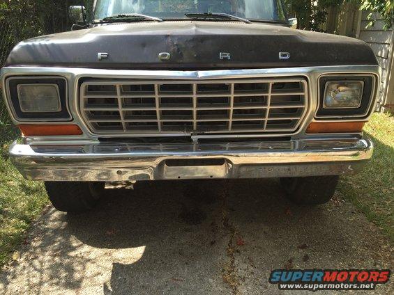 Dark colored Ford truck front grille and bumper, with orange turn signals. Tires visible