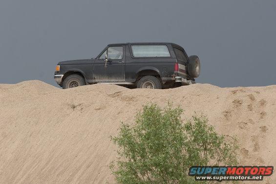 Black 1987 Ford Bronco parked on a sand dune with a spare tire on the back