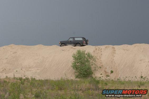 Dark 1987 Ford Bronco on a sand dune under a cloudy sky