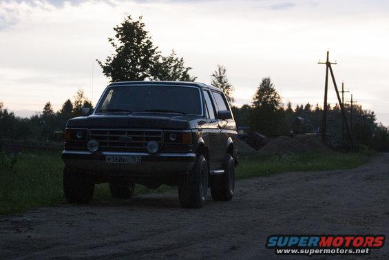 Dark 1987 Ford Bronco parked on a dirt road with trees and utility poles in the background