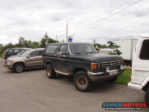 Dark 1987 Ford Bronco with gold rims and side steps parked on asphalt