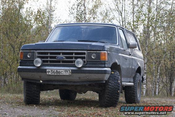 1987 Ford Bronco parked on a dirt road with trees in the background