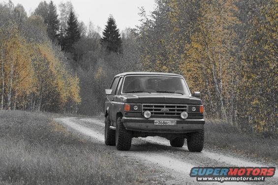 1987 Ford Bronco driving on a dirt road through autumn trees