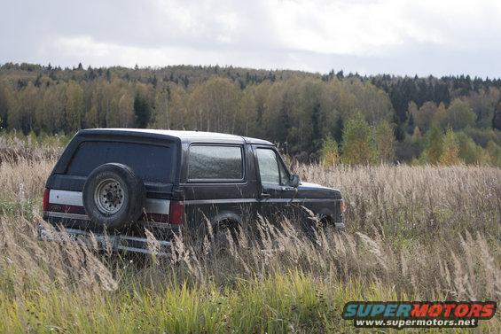 Black 1987 Ford Bronco parked in tall dry grass with a spare tire on the rear door