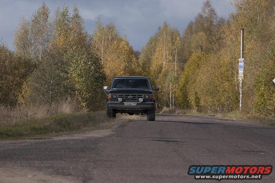 Front view of a black 1987 Ford Bronco on a road with autumn trees