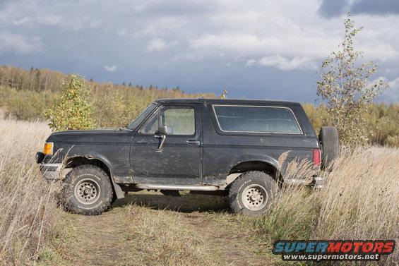 Black Ford Bronco parked on a dirt path in a grassy field with trees in the background