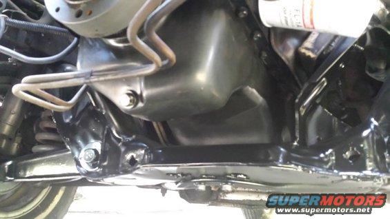 Underside view of a car's engine oil pan and suspension components. A white oil filter is visible