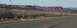 1990 Ford Bronco - A vast desert landscape unfolds under a hazy sky, with distant red rock formations and a paved road in the foreground.