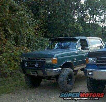 Green Ford Bronco with a brush guard and off-road tires parked next to a blue truck