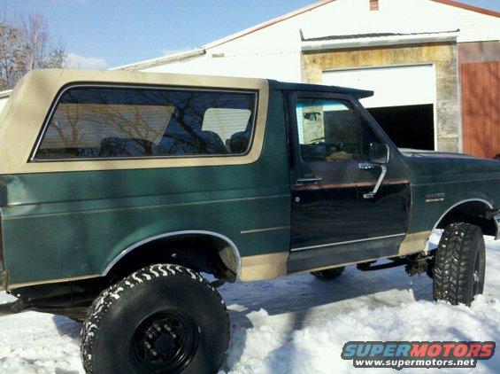 Green Ford Bronco with tan trim in snow, side view