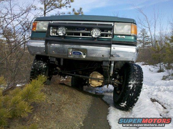 Green 1990 Ford Bronco front view on rocky, snowy terrain