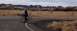 1990 Ford Bronco - Person and bicycle on road in desert with rocky formations. "SUPERMOTORS" logo visible.